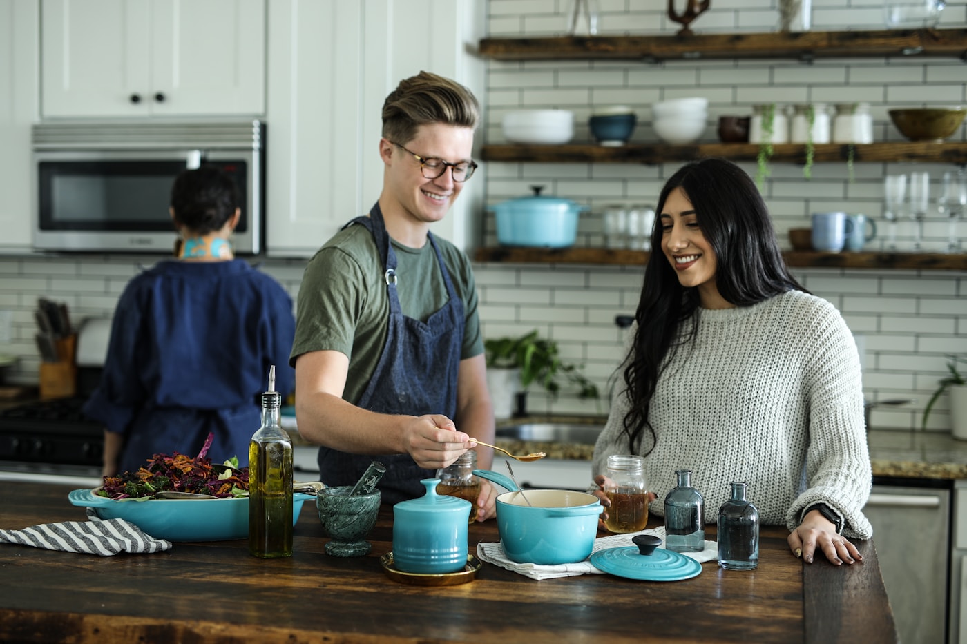 A few people gathered around a kitchen island, cooking and serving food together from a big pot