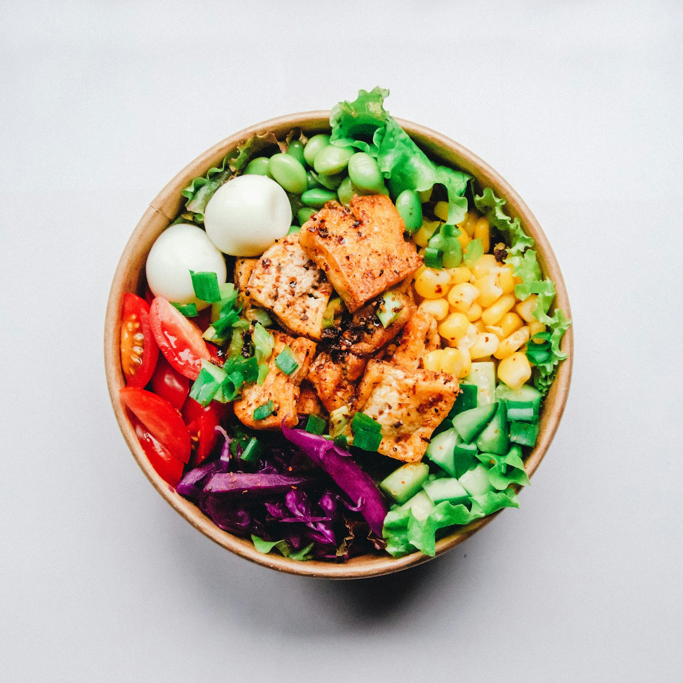 A colorful, fully prepared takeaway meal bowl of greens, roasted protein, corn and tomatoes, ready to hand out