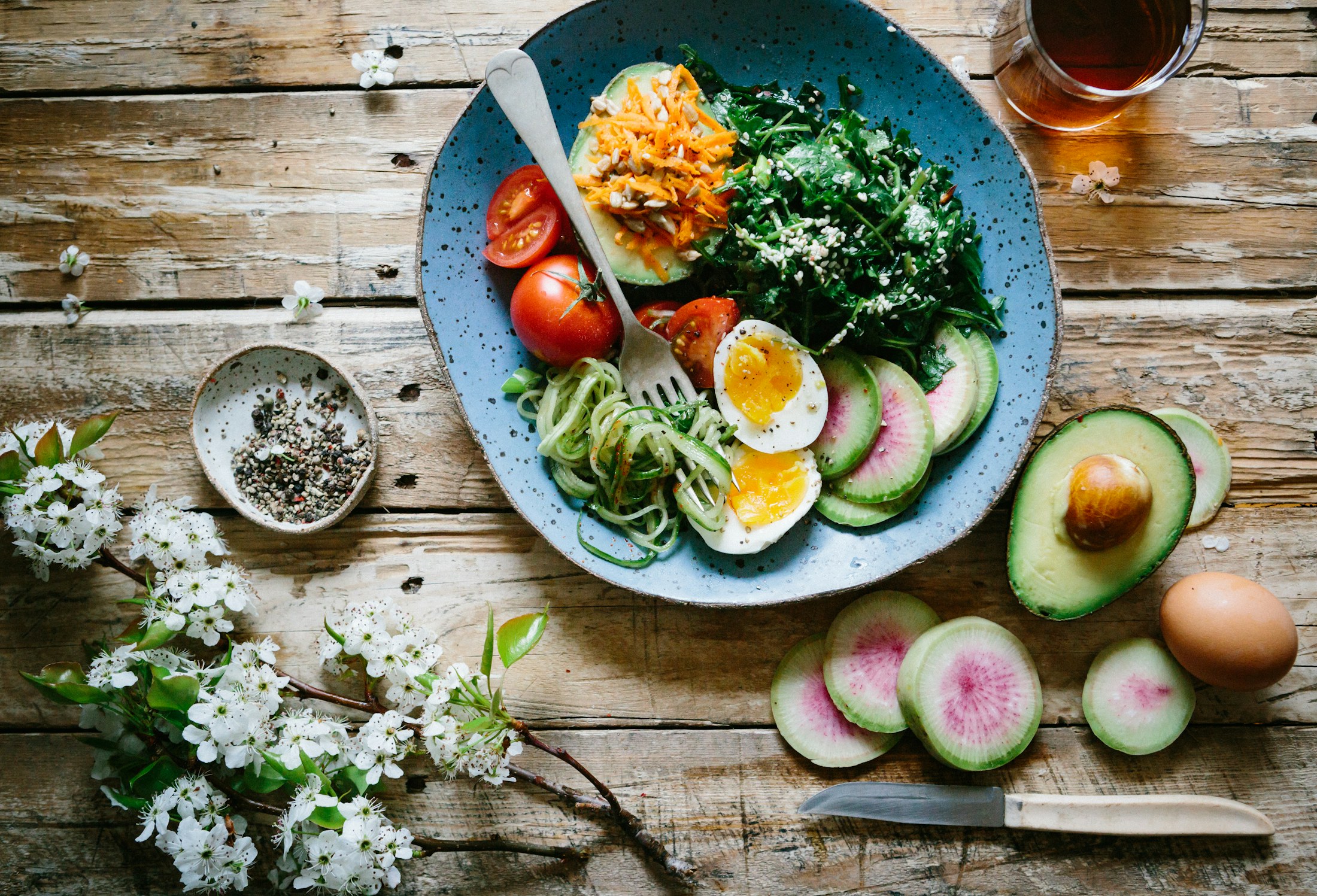 An overhead view of a rustic wooden table with a generous, colorful bowl of fresh food and warm morning light