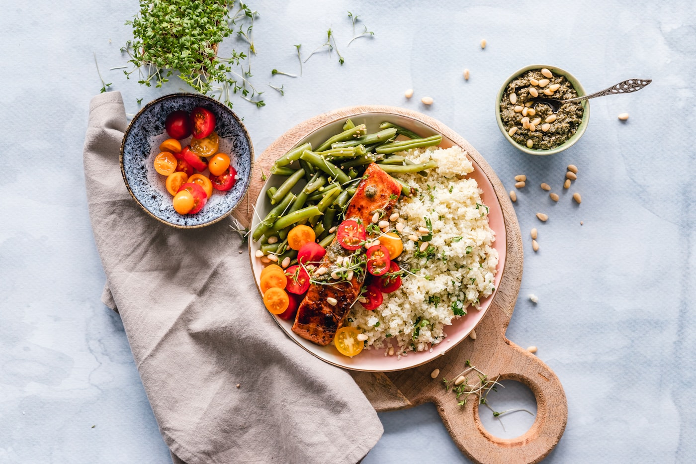 A freshly prepared bowl of grains, roasted vegetables, green beans and bright cherry tomatoes on a light table
